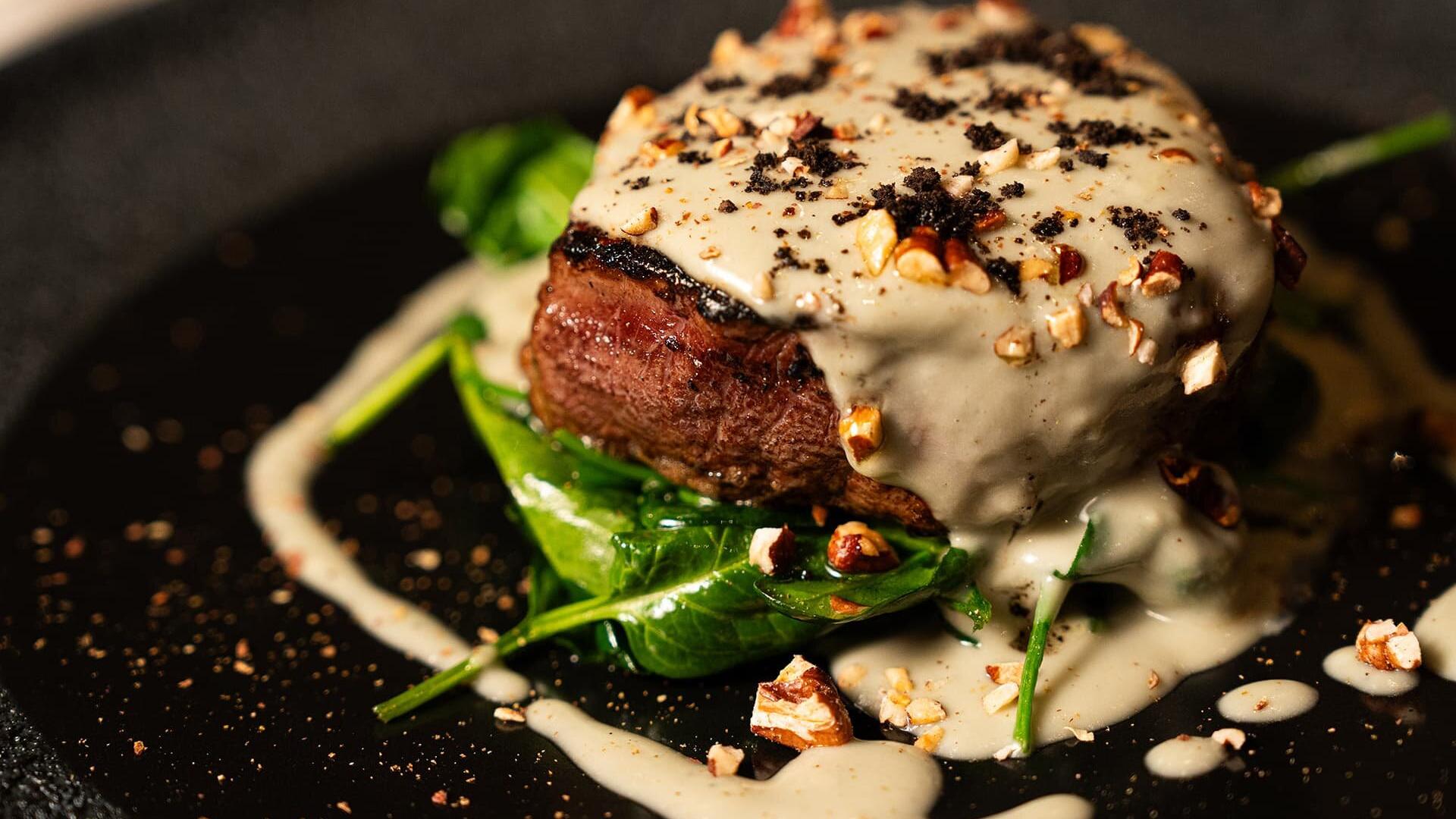 Succulenta bistecca con crema vellutata, spinaci freschi e croccanti noci su piatto elegante.