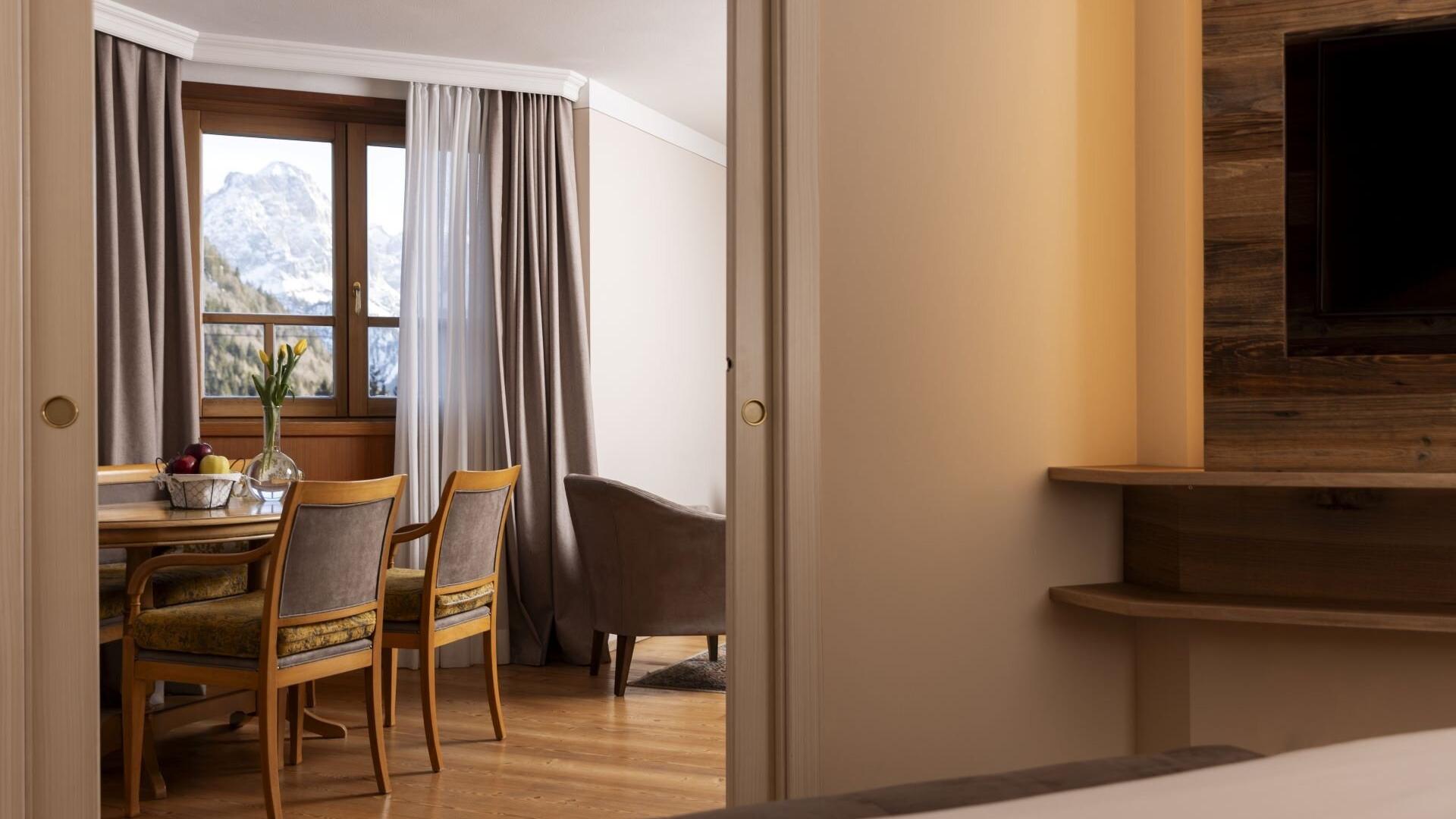 Interno elegante con vista montagna, tavolo con fiori, atmosfera calda e accogliente.