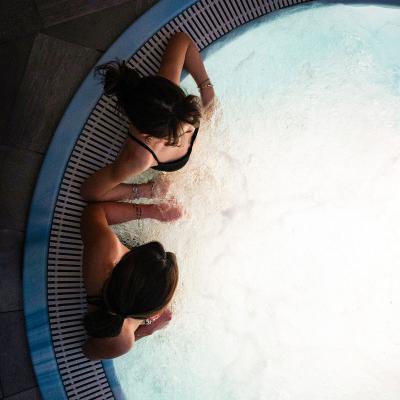 Due persone rilassano in una vasca idromassaggio, circondate da acqua scintillante.