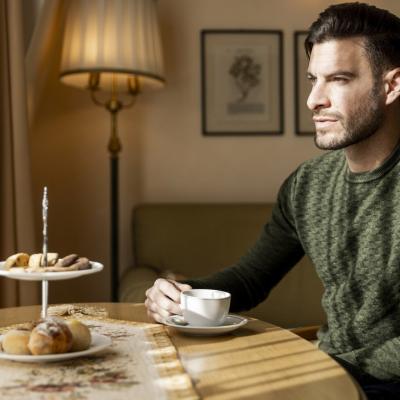 Uomo riflessivo beve caffè, dolci su tavolo, atmosfera calda e accogliente.