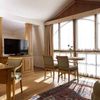 Accogliente stanza in legno con luce calda, tavolo, poltrone e finestra ampia.