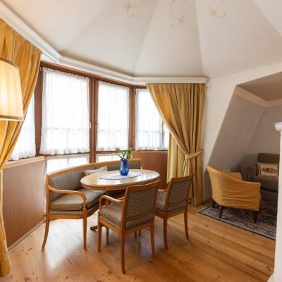 Accogliente salotto con tavolo, sedie eleganti, tende dorate e luce calda, atmosfera intima.