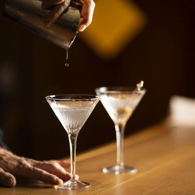 Mano versa cocktail in bicchieri eleganti, atmosfera calda e sofisticata.