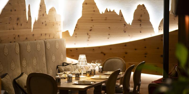 Ristorante elegante, tavolo apparecchiato, parete in legno con profilo montuoso illuminato.