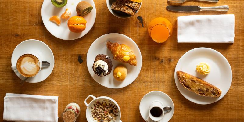 Colazione invitante: frutta fresca, croissant, dolci, caffè e succo d'arancia su tavolo rustico.