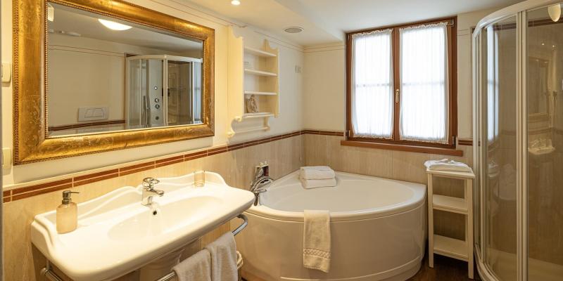 Bagno elegante con vasca angolare, specchio dorato e luce calda, accogliente e raffinato.