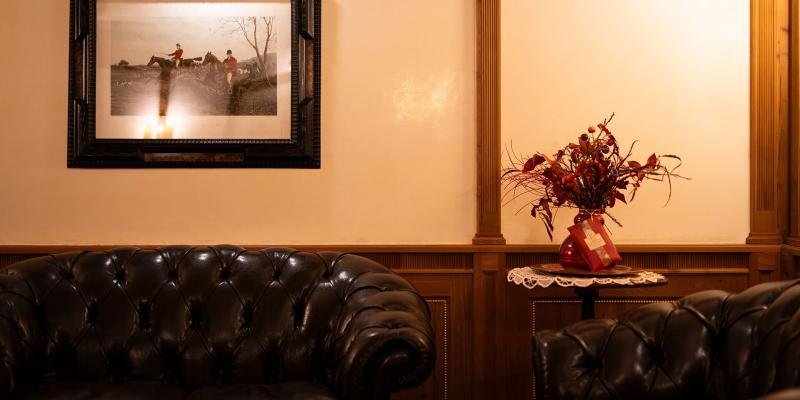 Salotto elegante con divani in pelle, quadro di caccia e fiori secchi su tavolino.