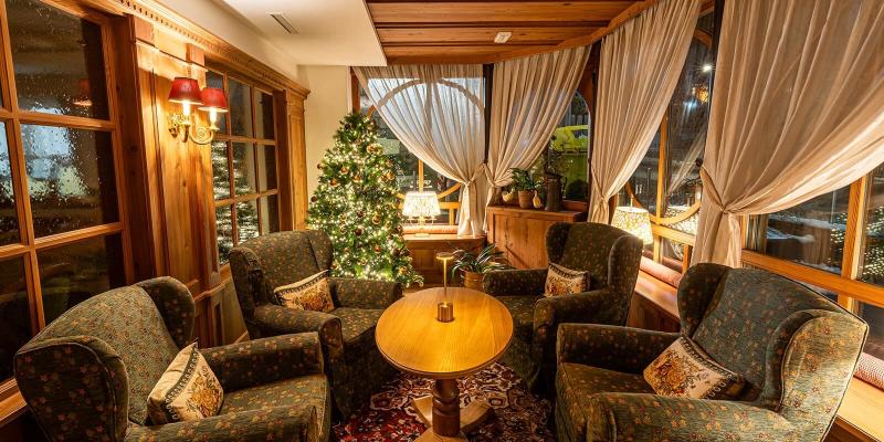 Salotto accogliente con poltrone, albero di Natale illuminato, atmosfera calda e serena.
