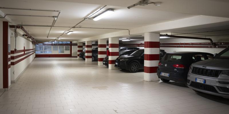 Parcheggio sotterraneo silenzioso, illuminato, con auto parcheggiate e colonne a strisce rosse.