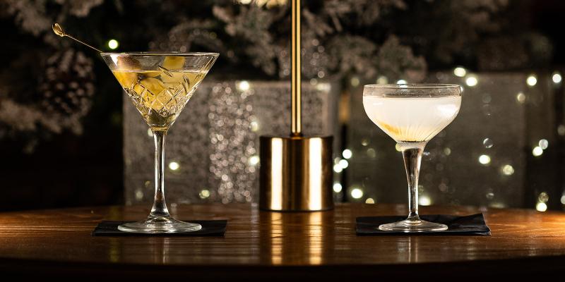 Due cocktail eleganti su un tavolo, atmosfera calda e festosa con luci scintillanti.