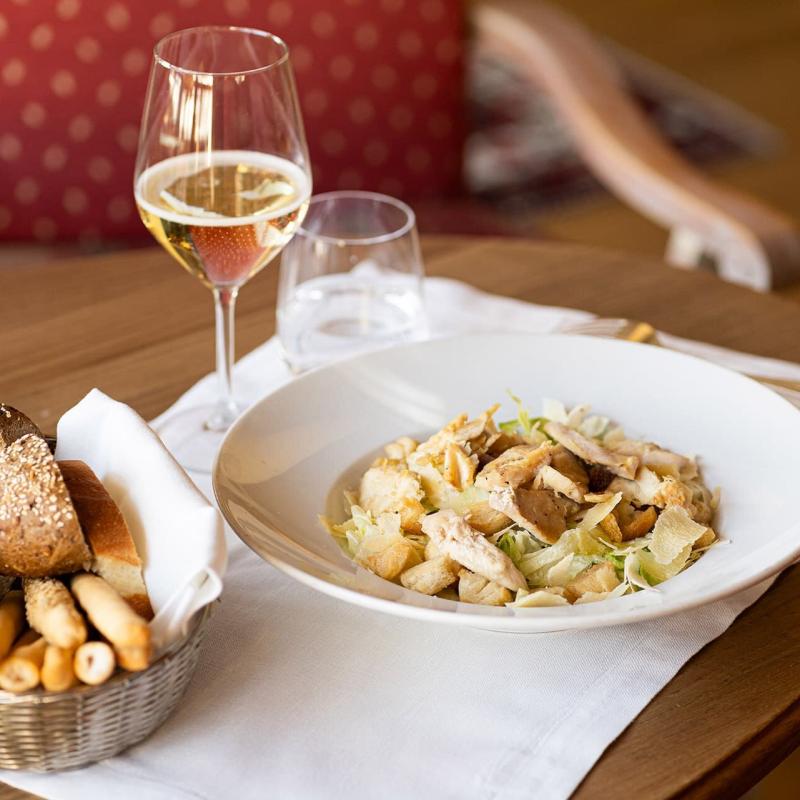 Elegante tavola imbandita con insalata di pollo, pane assortito e calice di vino frizzante.