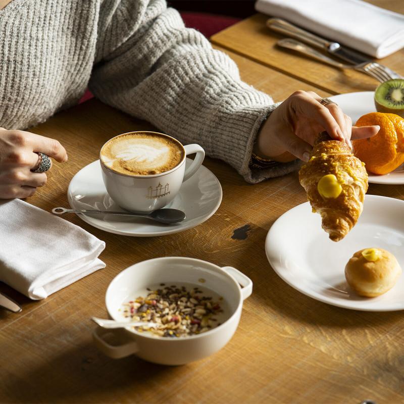 Colazione accogliente: cappuccino, croissant, frutta fresca e muesli su tavolo di legno.