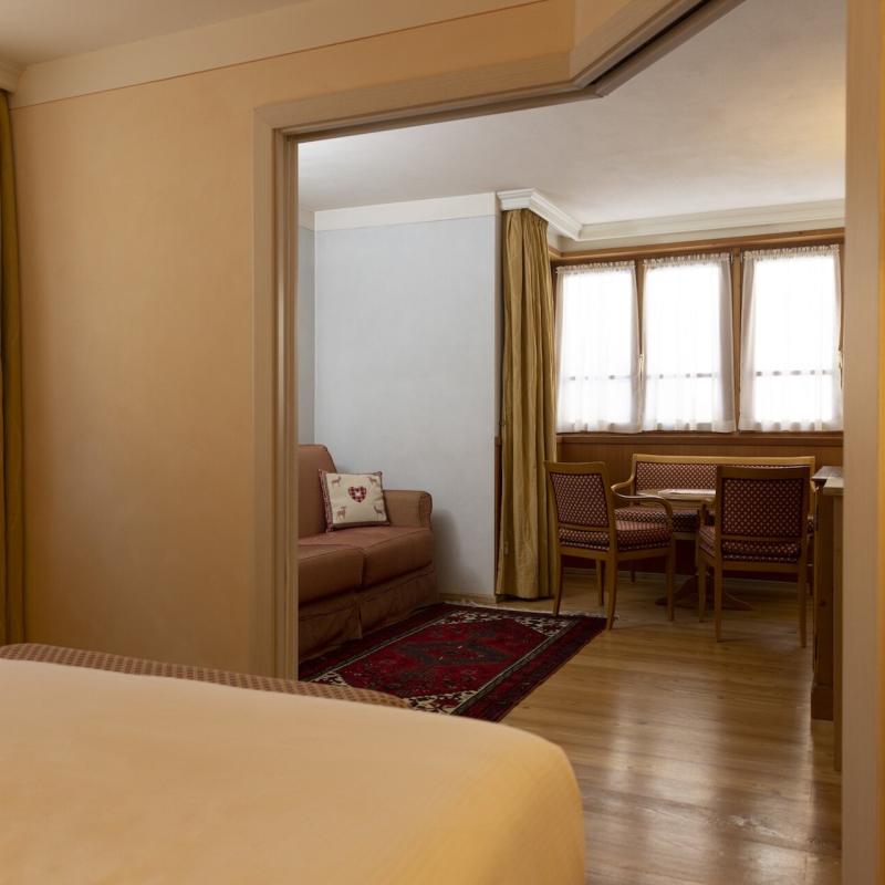 Interno accogliente con divano, tavolo e sedie, luce calda e tende dorate.
