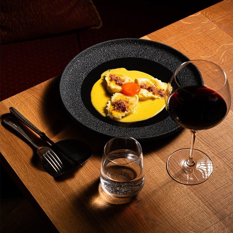 Piatto elegante di ravioli con crema, accompagnato da vino rosso, atmosfera intima e raffinata.
