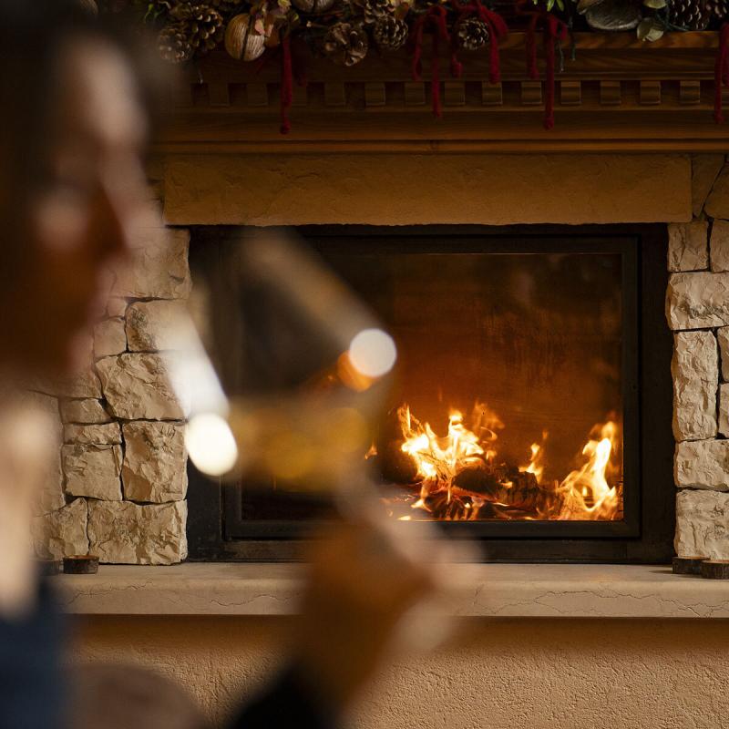 Un camino acceso, calore e intimità, con un bicchiere di vino in mano.